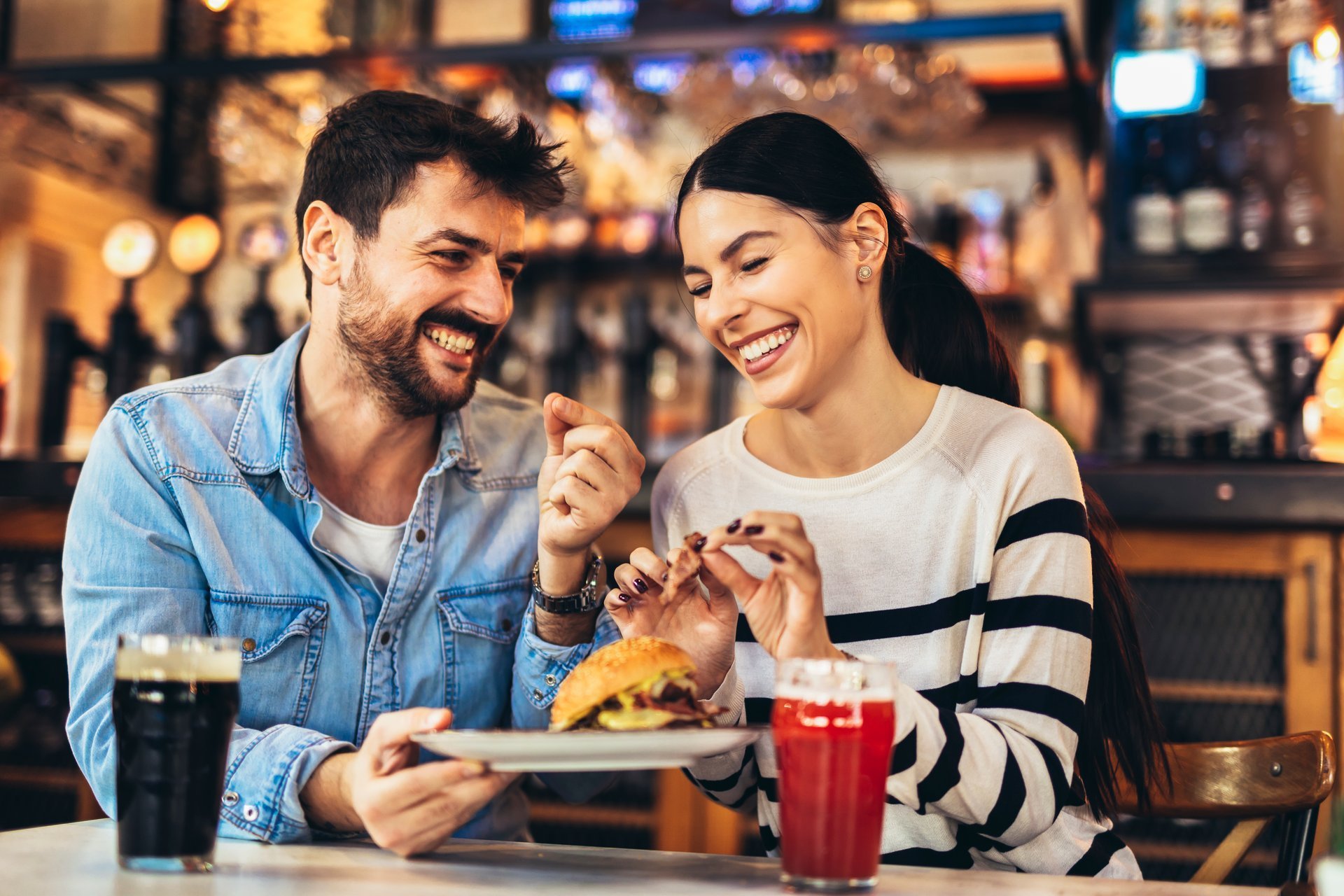 Young couple in love having fun spending leisure time together at restaurant, eating burgers and drinking beer